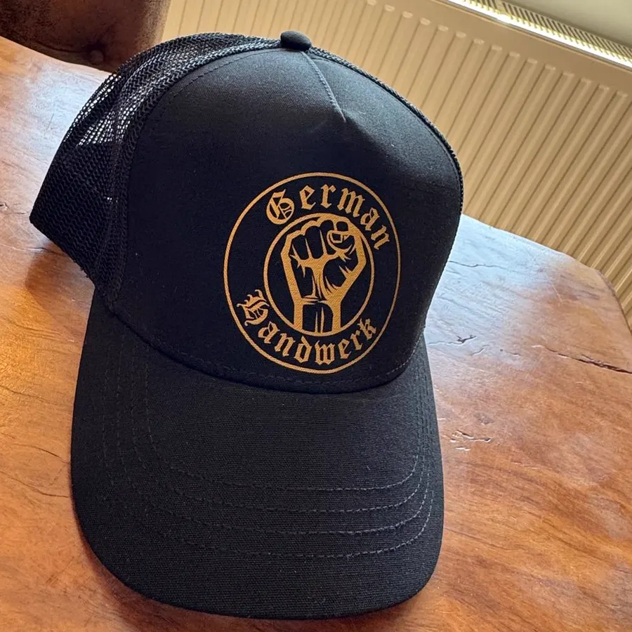 Schwarze Trucker-Cap mit goldenem Emblem auf dem Tisch.